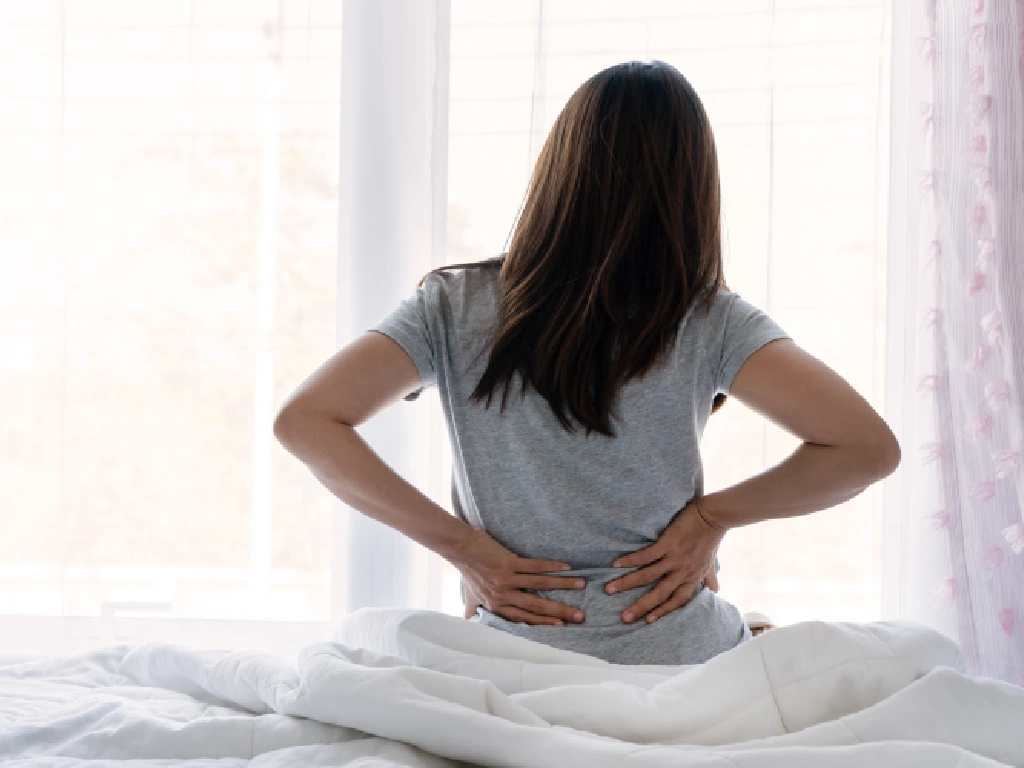 Young adult experiencing early joint pain warning signs while sitting on the bed